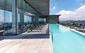 A rooftop pool with lounge chairs and a city view.