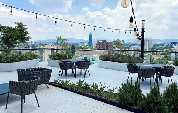 A rooftop terrace with outdoor seating, a city view, and string lights.