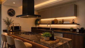 Una cocina moderna con una isla central, taburetes de bar, microondas, estufa, fregadero y un reloj en la pared.