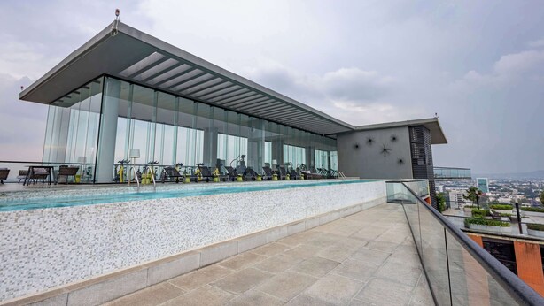 A modern building with a glass facade, a rooftop pool, and outdoor exercise equipment. - Minutes from Chapultepec & Downtown (Guadalajara)