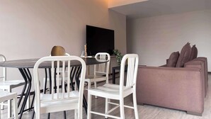 A modern living room with a dining area, a flat-screen TV mounted on the wall, and a sofa with cushions. - Minutes from Chapultepec & Downtown (Guadalajara)