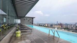 Ein Pool auf dem Dach mit Liegestühlen und Blick auf die Stadt.