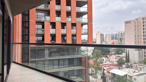 A modern building with a glass facade and red brick accents, featuring multiple balconies and a view of the cityscape. - Minutes from Chapultepec & Downtown (Guadalajara)