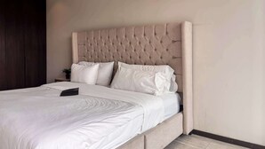 A neatly made bed with a tufted headboard, white bedding, and a small bedside table with a plant. - Minutes from Chapultepec & Downtown (Guadalajara)