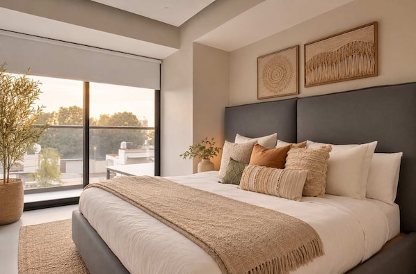A modern bedroom with a large bed, a view of the outdoors, and two wall-mounted artworks.