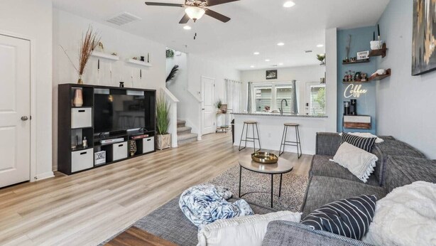 A modern living room with a TV, sofa, and coffee table. A staircase leads to a kitchen with bar stools. - Lakeside Paradise - Pflugerville (Pflugerville)