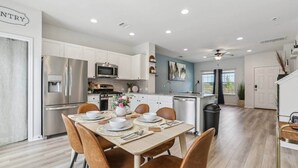 A modern kitchen with white cabinets, stainless steel appliances, and a dining area with a wooden table and brown chairs. - Lakeside Paradise - Pflugerville (Pflugerville)