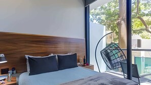 Moderni hotellihuone, jossa on suuri sänky, yöpöytä lampun kanssa ja suuret ikkunat, joista on näkymä ulos.