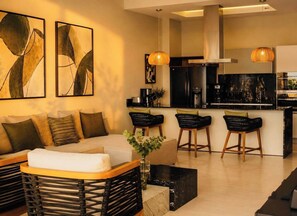 A modern living room with a sofa, a coffee table, and a kitchen area with a stove and bar stools.