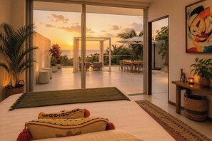 A modern bedroom with a large bed, a view of the outdoors, and a dining area with chairs and a table.