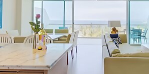 Enjoy a serene sea view from the DEL MAR room, featuring a dining table, sofa, and side table with a vase of flowers.