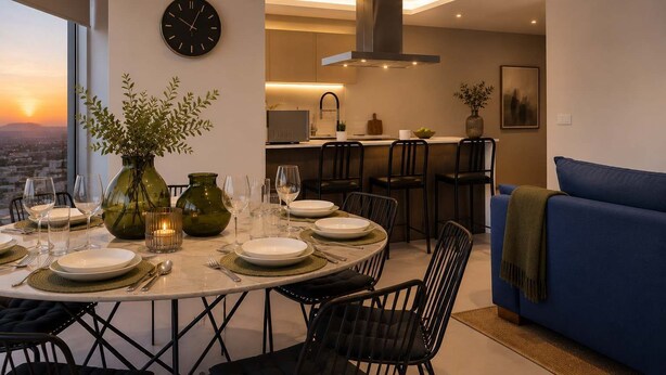 A dining area with a table set for four, a clock on the wall, and a city view through the window.