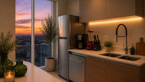 A modern kitchen with a stainless steel refrigerator, a coffee maker, and a sink. There is a view of a cityscape through a large window.
