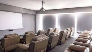 A room with rows of leather recliner chairs, a ceiling-mounted projector, and a blank screen on the wall.