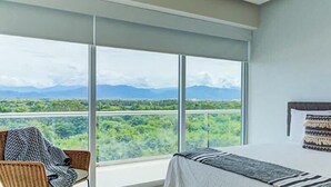 Un dormitorio con un amplio ventanal que ofrece vistas a un paisaje verde y montañas.