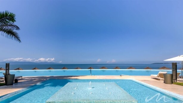 Una piscina infinita rectangular con vistas despejadas al océano, rodeada de sillones de descanso y sombrillas.