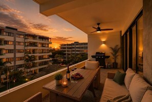 A balcony with a table, chairs, a sofa, a ceiling fan, and a grill.