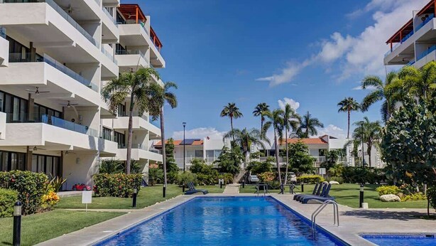 Ein modernes Hotel mit Swimmingpool, Palmen und blauem Himmel.