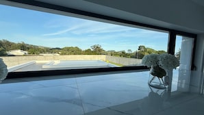 Um interior moderno com uma grande janela, uma mesa de vidro com um vaso de flores e vista para um terraço.