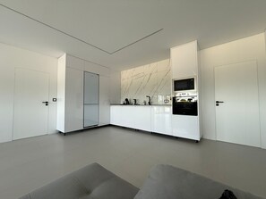 A modern kitchen with white cabinetry, a marble backsplash, and built-in appliances.