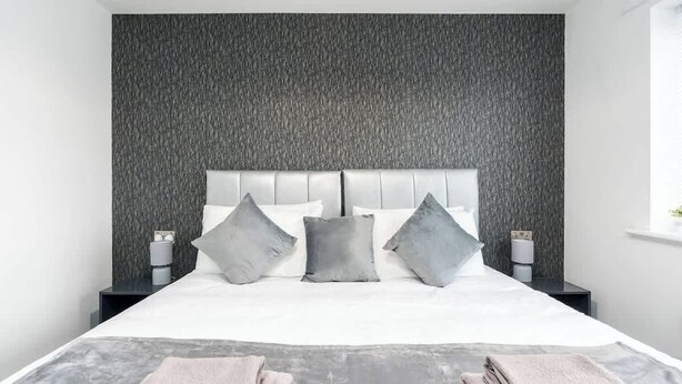 Une chambre d’hôtel moderne avec un grand lit, un mur gris à texture et deux tables de chevet avec des lampes.