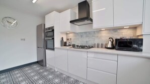 Une cuisine moderne avec des meubles blancs, une cuisinière en acier inoxydable, un four à micro-ondes et une bouilloire.