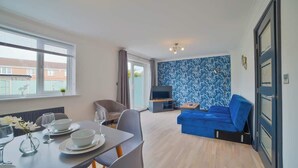 Un salon moderne comprenant un coin repas, un canapé bleu, un téléviseur et un mur décoré de motifs.