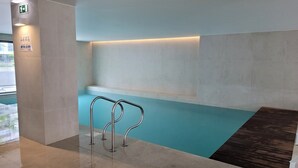 Ein moderner, überdachter Poolbereich mit deutlicher Beschilderung für Pool und Umkleideräume, mit Fliesenboden und einer Holzterrasse.