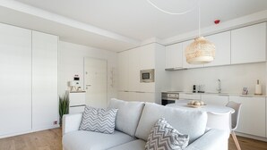 Ein modernes, minimalistisches Wohnzimmer mit grauem Sofa, einem Esstisch und einer Küchenzeile.