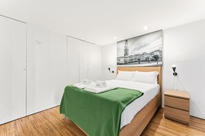 Ein Hotelzimmer mit Bett, grüner Decke, weißen Handtüchern, Nachttisch, Lampe und einem Wandbild.