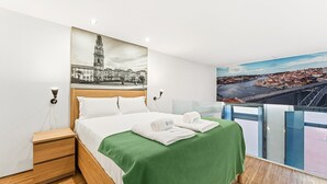 Habitación de hotel con cama, mesita de noche, manta verde y vistas a la ciudad.