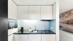 Una cocina compacta con muebles blancos, encimera negra y pileta de acero inoxidable.