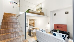 Habitación de hotel moderna con escalera de madera, cama en altillo, zona de comedor y televisor de pantalla plana.