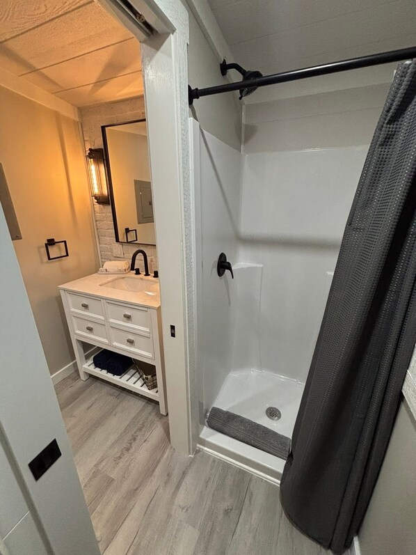 A bathroom with a white sink, a mirror, a shower with a black shower curtain, and a wooden floor.