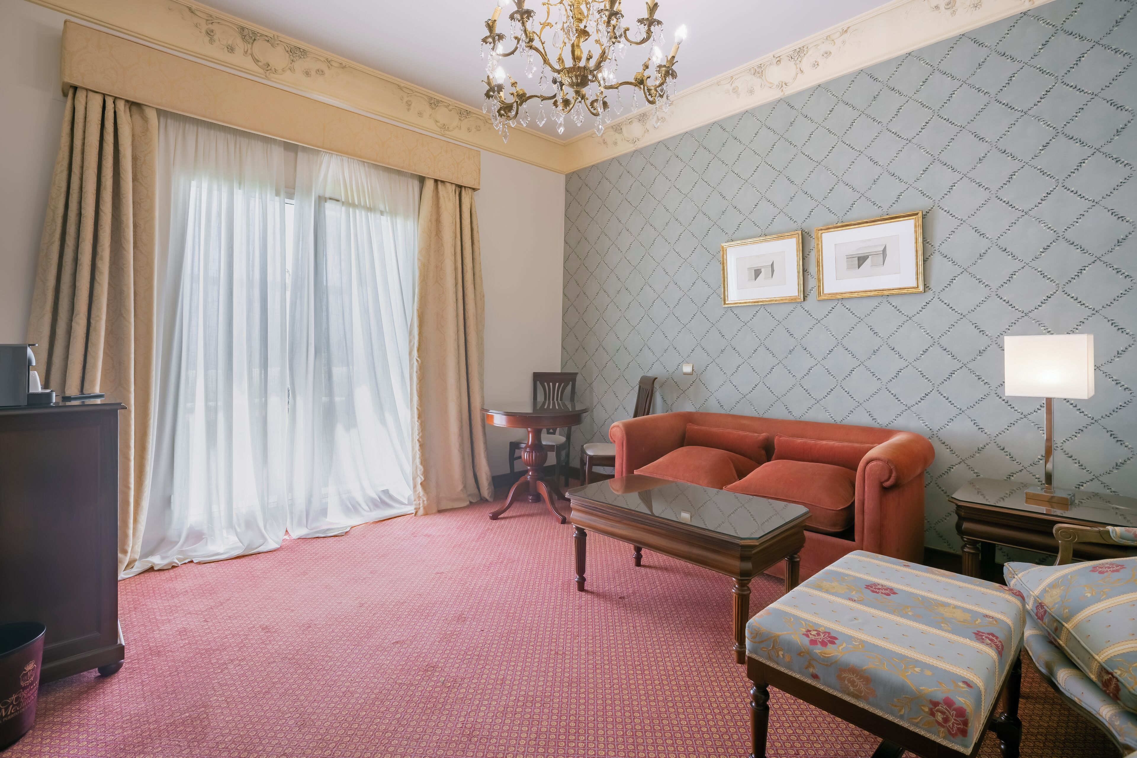 Een hotelkamer met een roodgekleurd tapijt, een bank, een salontafel, een televisie en een kroonluchter.