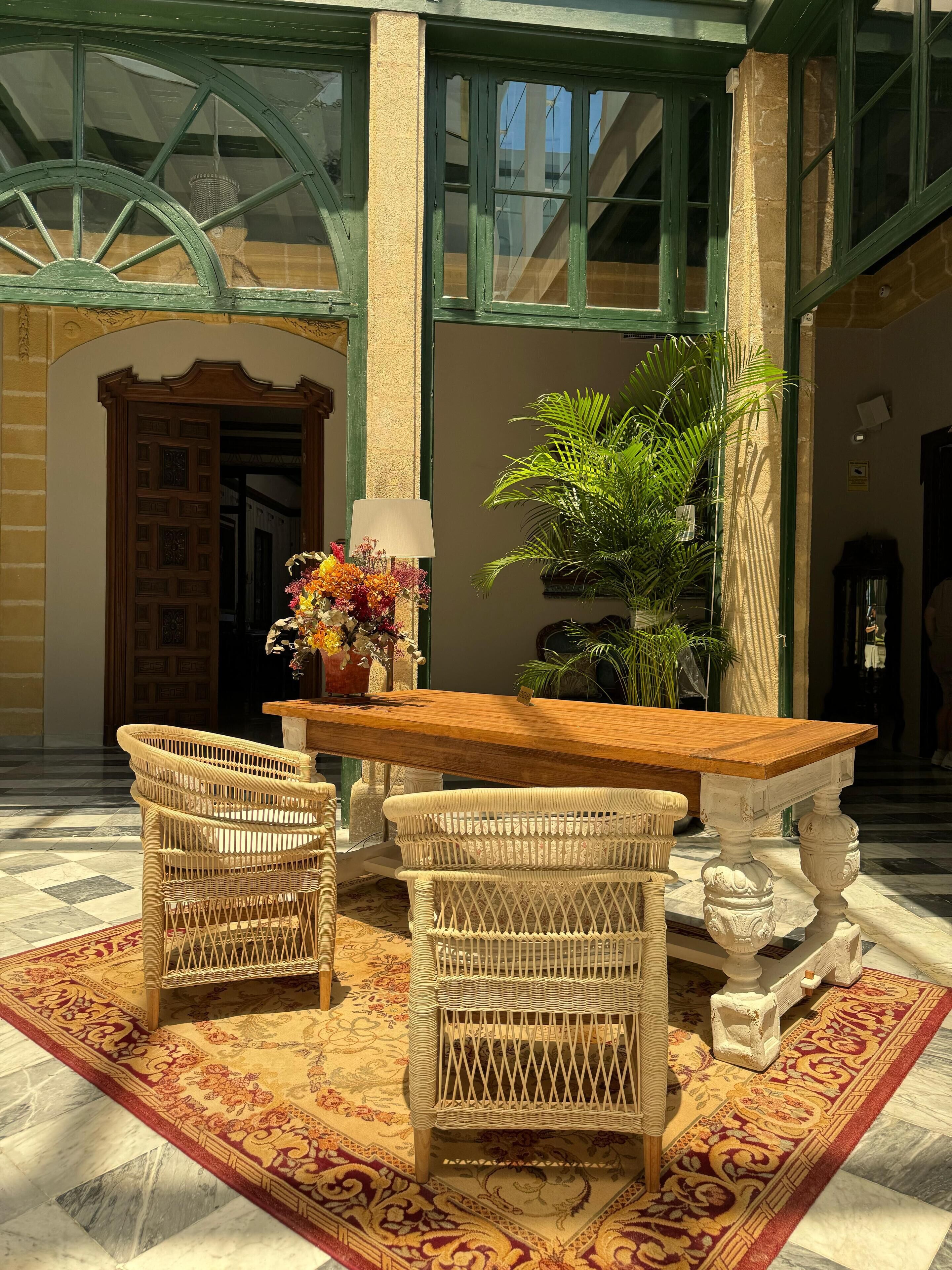 Un hall con una mesa de madera y sillas de mimbre, una planta en maceta y una alfombra estampada.