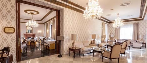 Un vestíbulo de hotel amplio y elegantemente decorado, con zona de comedor, diferentes opciones de asientos y candelabros decorativos.