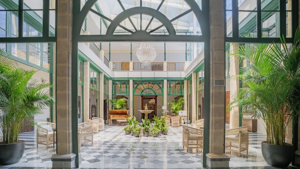 A spacious atrium with a checkered floor, large potted plants, and wicker furniture.