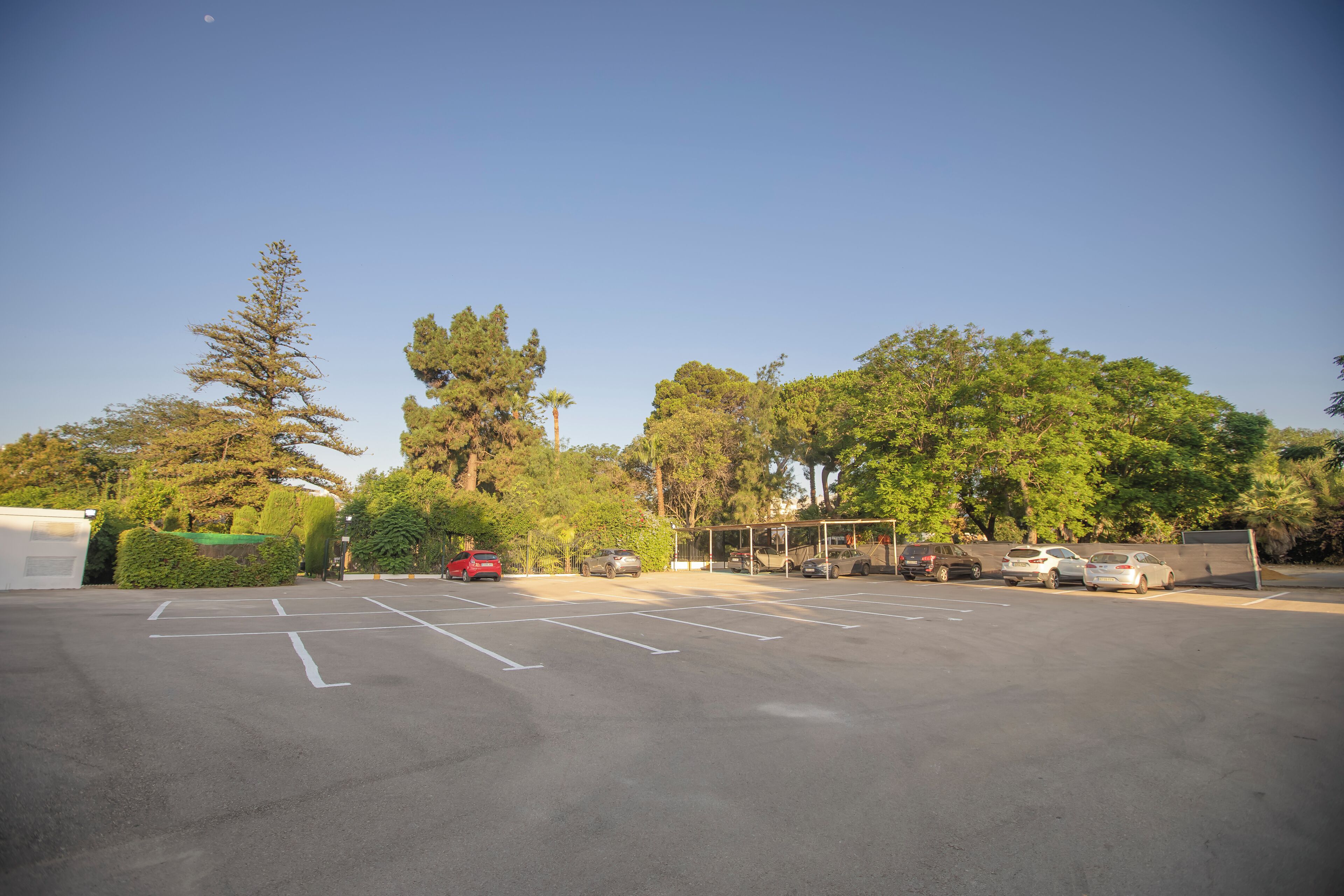 A parking lot with several cars, surrounded by trees and a clear sky.