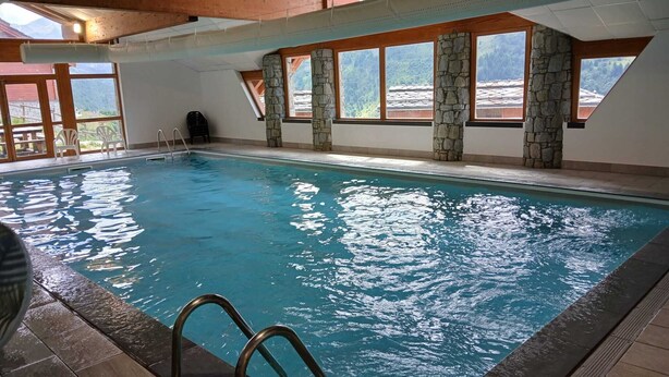 An indoor swimming pool with stone pillars and large windows. - GREEN THISTLE (Valmeinier)