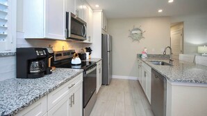 A modern kitchen with white cabinets, stainless steel appliances, granite countertops, and a clock on the wall. - Relax in Peaceful Paradise at Sanibel Arms West Unit A1 -close to the Beach (Sanibel)
