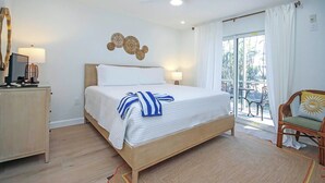 A hotel room with a bed, bedside lamps, a desk, and a view of the outdoors. - Sanibel Arms West Newly Renovated Unit A2 First Floor Garden View (Sanibel)