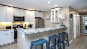 A modern kitchen with white cabinets, stainless steel appliances, a granite countertop, and blue bar stools. - Coastal Accents and Charm (Sanibel)