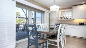A modern kitchen with white cabinets, a dining area with a glass table, and a view of the outdoors. - Coastal Accents and Charm (Sanibel)