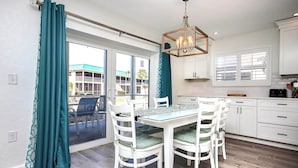 A modern kitchen with white cabinets, a dining table with chairs, and a view through the glass door. - Cheerful Unit B1 Sanibel Arms West | Just a 2 Minute Walk to the Beach (Sanibel)