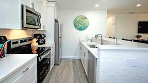 A modern kitchen with white cabinetry, stainless steel appliances, and a central island with a sink. - Cheerful Unit B1 Sanibel Arms West | Just a 2 Minute Walk to the Beach (Sanibel)