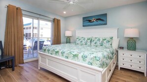 Un dormitorio con cama, mesita de noche, lámpara, ventilador de techo y ventana con cortinas.