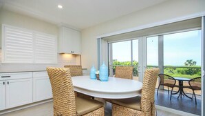 A dining area with wicker chairs, a round table, and a view of greenery through large sliding glass doors. - Radiant Unit C4 · Sanibel Arms West | Gulffront Panoramic Gulf Views (Sanibel)