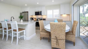 A modern kitchen with white cabinetry, stainless steel appliances, and a central island with seating. - Radiant Unit C4 · Sanibel Arms West | Gulffront Panoramic Gulf Views (Sanibel)