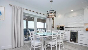 A modern kitchen with white cabinetry, a glass dining table, and a built-in coffee machine. - Spectacular Unit C5 · Sanibel Arms West | Gulffront Endless Gulf Views (Sanibel)